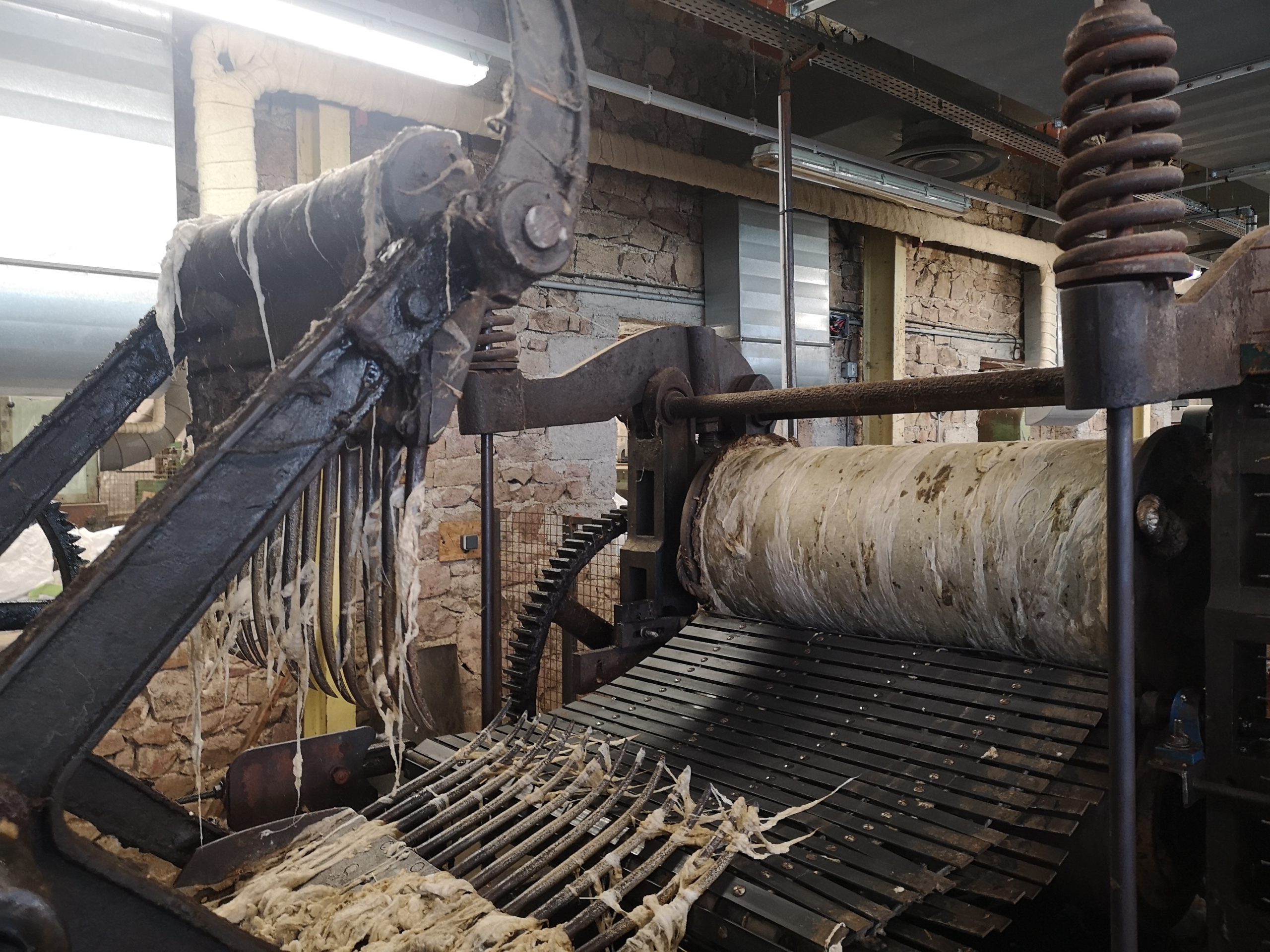 Vue rapprochée d'une ancienne machine industrielle traitant des matières fibreuses à l'intérieur d'une usine rustique aux murs de pierre.
